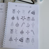 Notebook with Christmas advent calendar-christmas themed doodles on a white surface with decorative items.