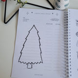 Notebook with a Christmas tree outline on a white surface with decorative items.